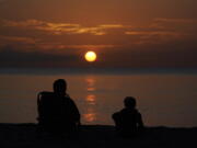 FILE - A pair of beach goers watch the sun rise over the Atlantic Ocean, Friday, June 10, 2022, in Surfside, Fla. All the experts predicted this would be a more active than normal hurricane season, but then nothing happened. Scientists think a persistent patch of dry air is the reason storms aren't forming.