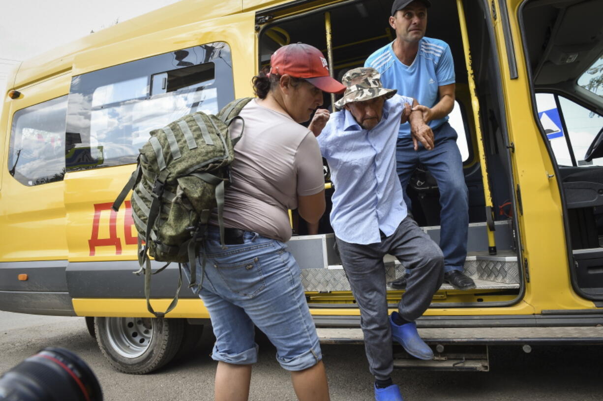 People help evacuate an elderly man from an area near the site of explosion at an ammunition storage of Russian army near the village of Mayskoye, in Crimea, Tuesday, Aug. 16, 2022.