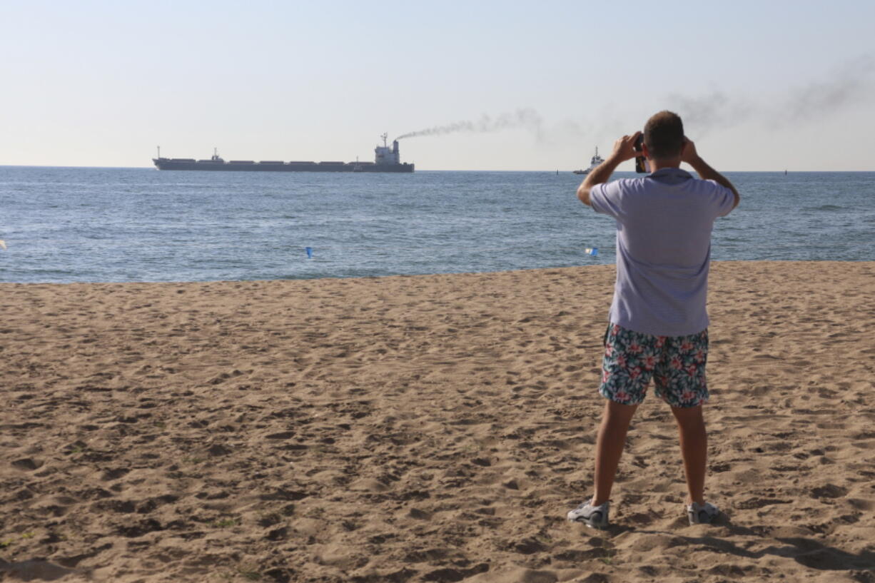 A man takes a picture as the Glory bulk carrier makes its way from the port in Odesa, Ukraine, Sunday, Aug. 7, 2022. According to Ukraine's Ministry of Infrastructure, the ship under the Marshall Islands' flag is carrying 66 thousand tons of Ukrainian corn.