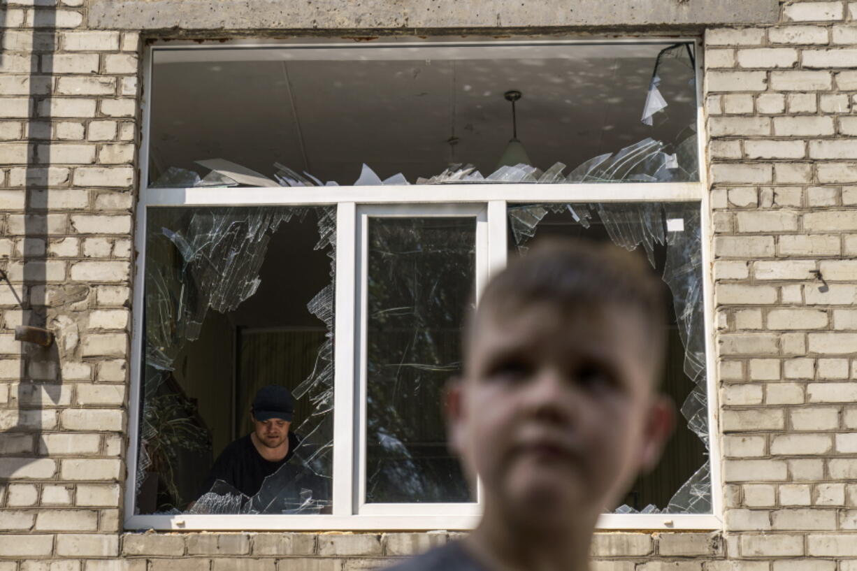 A worker cleans up inside as Tikhon Pavlov, 11, walks past the Kramatorsk College of Technologies and Design, where he used to take karate lessons, after an early morning rocket attack in Kramatorsk, Donetsk region, eastern Ukraine, Friday, Aug. 19, 2022. Russia continued to shell towns and villages in Ukraine's embattled eastern Donetsk region, according to regional authorities, where Russian forces are pushing to overtake areas still held by Ukraine.