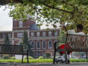 FILE - With the Founders Library in the background, a young man reads on Howard University campus July 6, 2021, in Washington. For millions of Americans, President Joe Biden'??s student loan cancellation offers a life-changing chance to escape the burden of debt. But for future generations of students, it doesn't fix the underlying reason for the crisis: the rising cost of college.