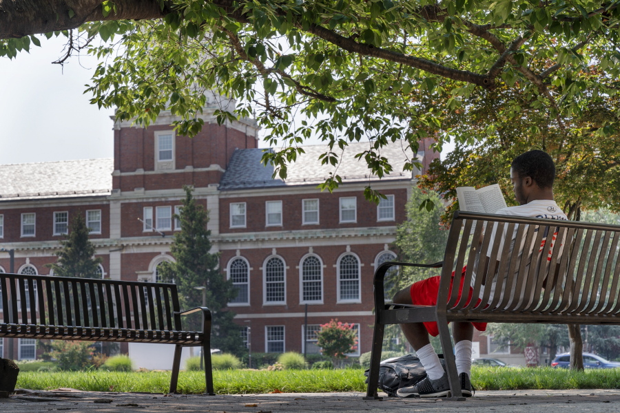 FILE - With the Founders Library in the background, a young man reads on Howard University campus July 6, 2021, in Washington. For millions of Americans, President Joe Biden'??s student loan cancellation offers a life-changing chance to escape the burden of debt. But for future generations of students, it doesn't fix the underlying reason for the crisis: the rising cost of college.