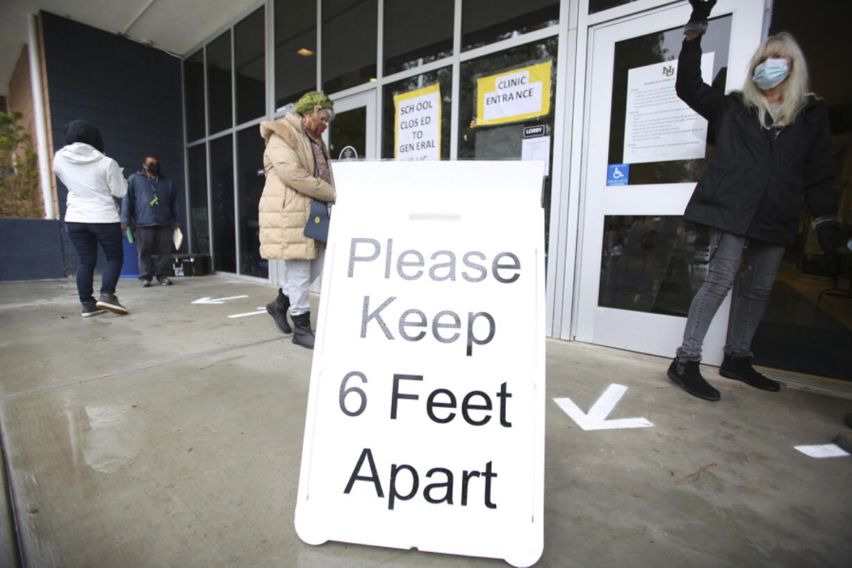 FILE - A sign asks those getting vaccinated to keep 6 feet apart during the vaccination event, Wednesday, Jan. 27, 2021, at Nevada Union High School in Grass Valley, Calif. The CDC has again revised its COVID guidelines, further relaxing quarantine recommendations and dropping the recommendation that people stay at least 6 feet away from each other.