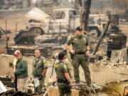 Sheriff's Deputy Johnson stands at a burned home as search and rescue workers recover the remains of a McKinney Fire victim on Monday, Aug. 1, 2022, in Klamath National Forest, Calif.