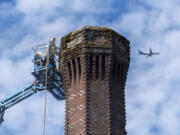 An airplane passes overhead as workers begin the brick-by-brick demolition of Providence Academy's smokestack on Wednesday. Construction workers anticipate removing the tower's top 20 feet by the end of Thursday or Friday morning.