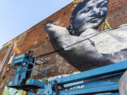 Artist Mario De Leon, left, takes a cherry picker up to work on his mural of Spanish Romani flamenco dancer and singer Carmen Amaya on Washington Street. The mural is part of the Great River Arts Festival, happening now through Oct. 10.