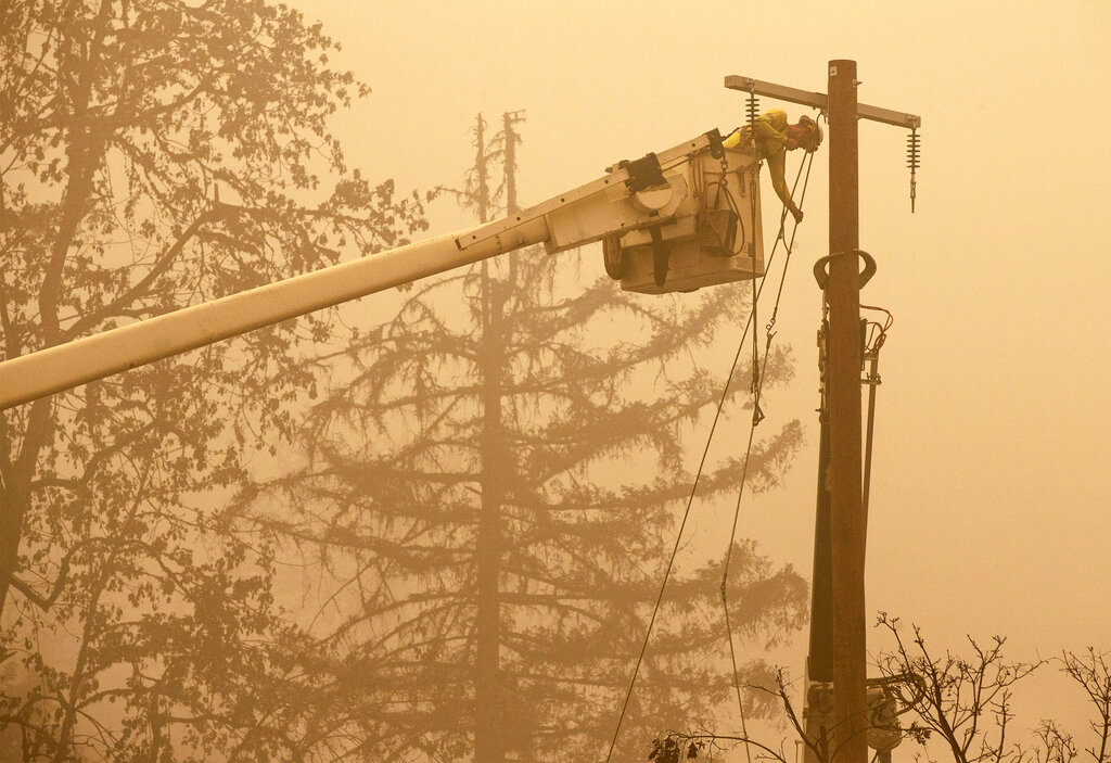 FILE - Workers continue to repair the power system after flames from the Beachie Creek Fire burned through Fishermen's Bend Recreation in Mill City, Ore., on Sept. 13, 2020. Oregon utilities began shutting down power to thousands of customers on Friday, Sept. 9, 2022, as dry easterly winds swept into the region, raising the risk of wildfire danger. Portland General Electric halted power in the Columbia River Gorge and around Mount Hood and a second power company was poised to do the same Friday.