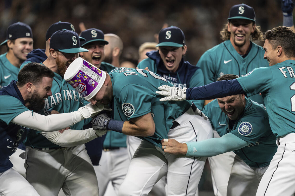 Seattle Mariners including Jesse Winker, left; Ty France, third from right; Logan Gilbert, second from right; and Adam Frazier, right celebrate a home run by Cal Raleigh in ninth inning of a baseball game against the Oakland Athletics, Friday, Sept. 30, 2022, in Seattle. The Mariners won 2-1 to clinch a spot in the playoffs.