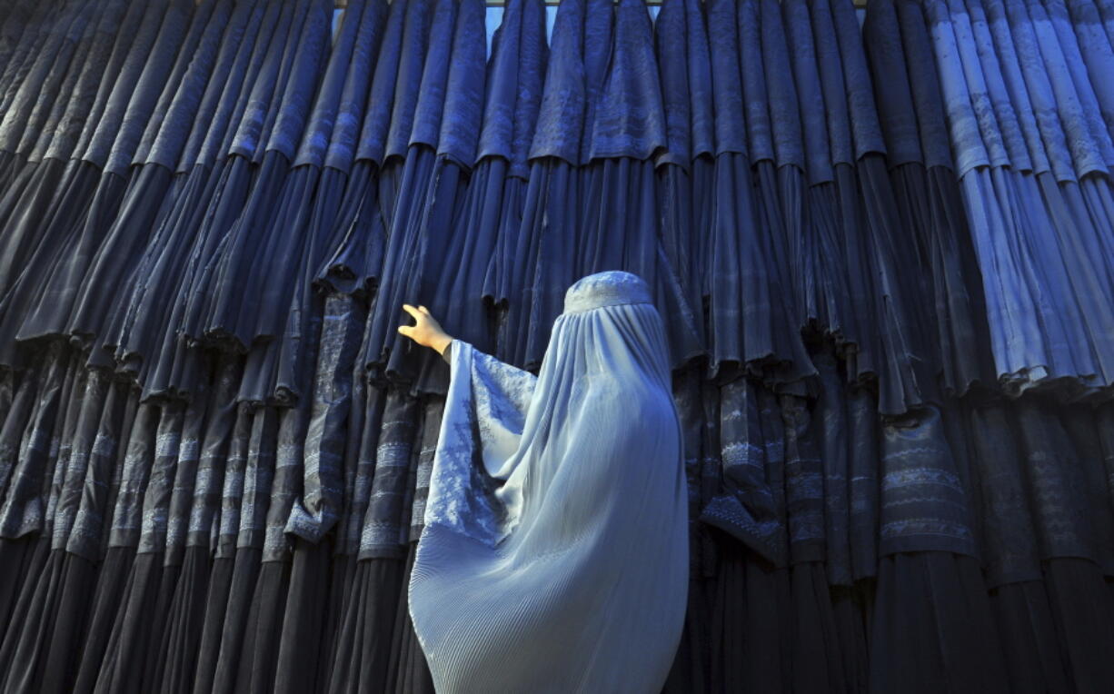 FILE - A woman clad in a burqa looks at other pieces of Afghanistan's traditional, all-encompassing dress at a store in Mazar-i Sharif, north of Kabul, Afghanistan, on Sept. 10, 2015. The Taliban announced they have arrested and will soon sentence an Afghan woman who appeared in a video on social media on Aug.  30, 2022, and said a senior Taliban official forced her into marriage and raped her repeatedly.