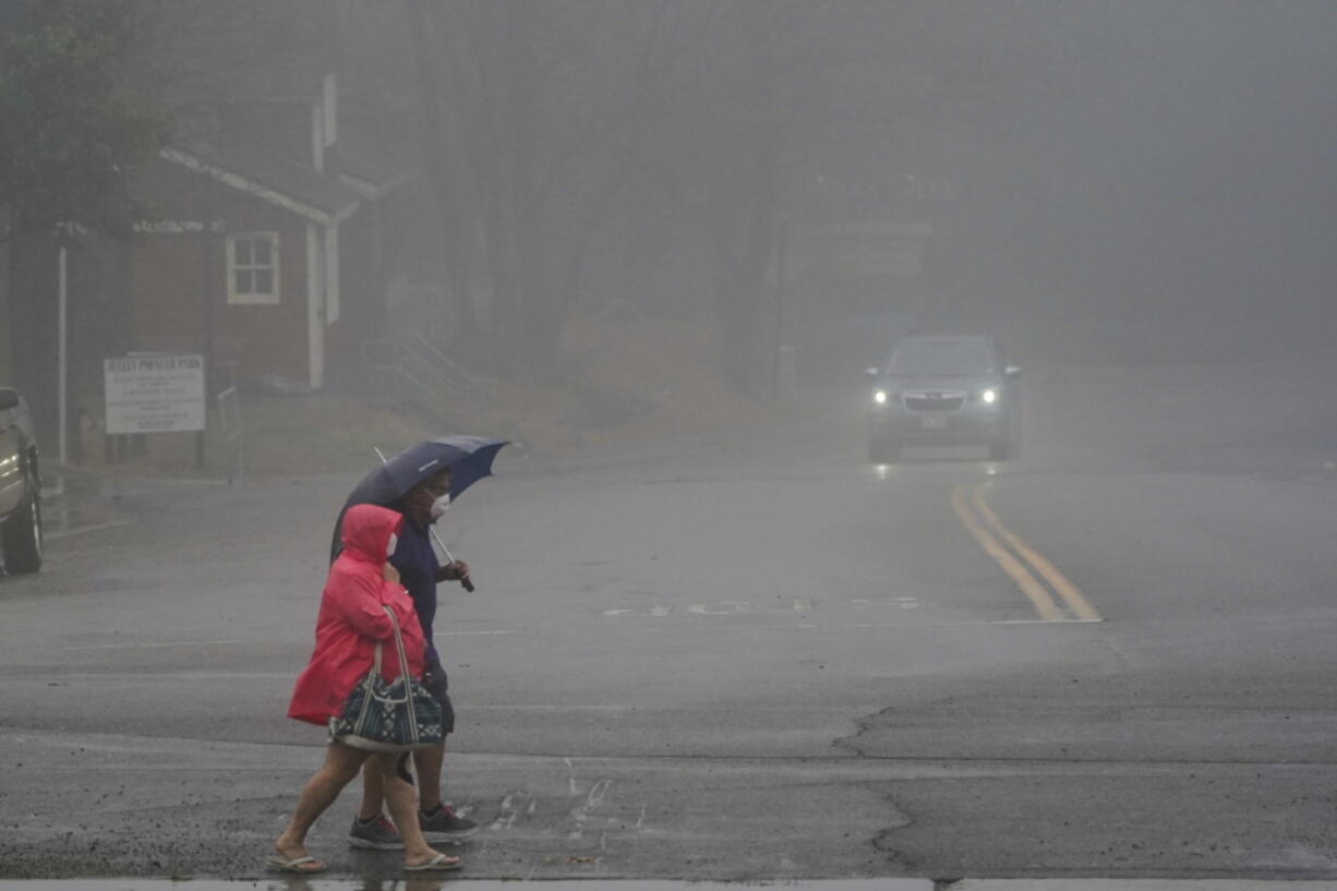 Two people cross the road as wind and rain pummel the area Friday, Sept. 9, 2022, in Julian, Calif. A tropical storm nearing Southern California has brought fierce mountain winds, high humidity, rain and the threat of flooding to a region already dealing with wildfires and an extraordinary heat wave.