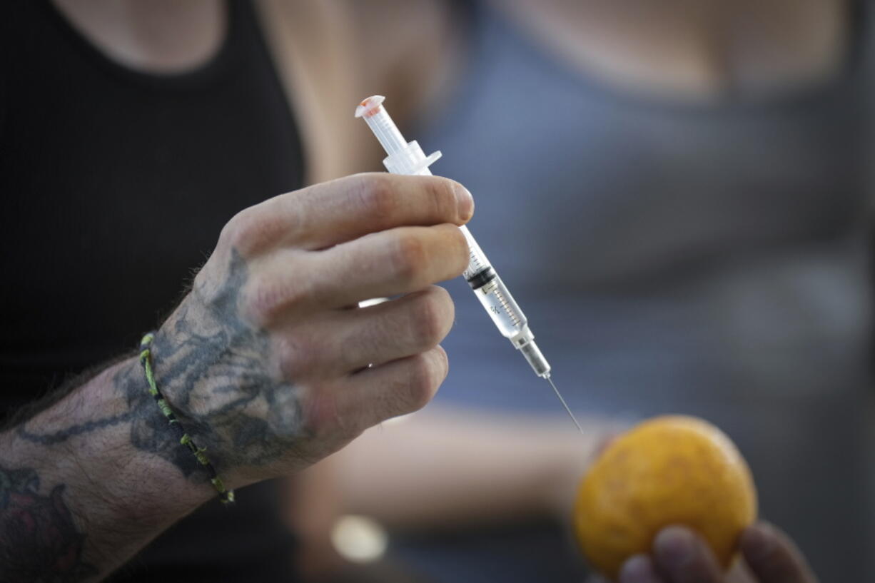 A person holds a syringe and an orange while learning how to administer Naloxone to an overdose victim, during an International Overdose Awareness Day gathering in Surrey, British Columbia, on Wednesday, Aug. 31, 2022.