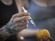 A person holds a syringe and an orange while learning how to administer Naloxone to an overdose victim, during an International Overdose Awareness Day gathering in Surrey, British Columbia, on Wednesday, Aug. 31, 2022.