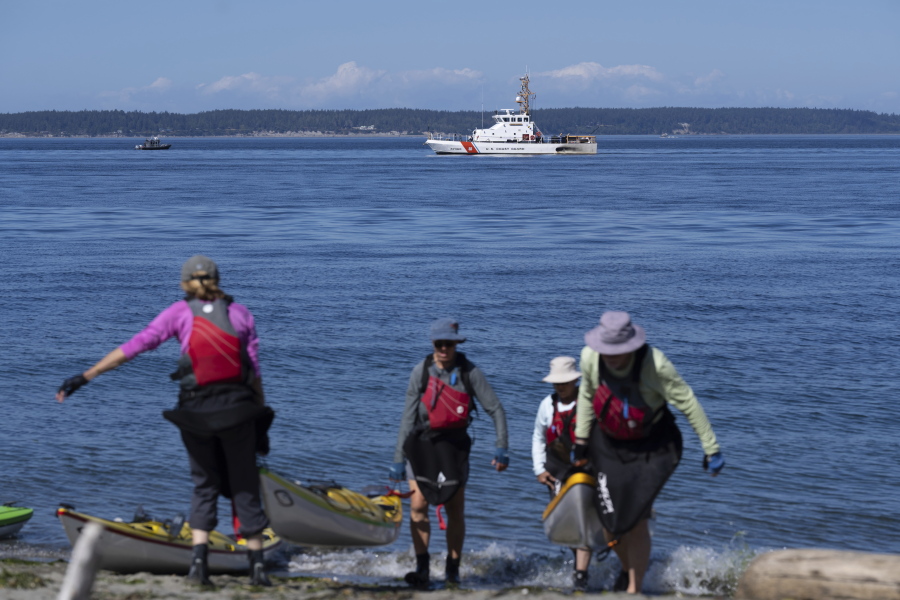 A U.S. Coast Guard boat searches the area Monday, Sept. 5, 2022, as kayakers pull out, near Freeland, Wash., on Whidbey Island north of Seattle where a chartered floatplane crashed the day before. The plane was carrying 10 people and was en route from Friday Harbor, Wash., to Renton, Wash.