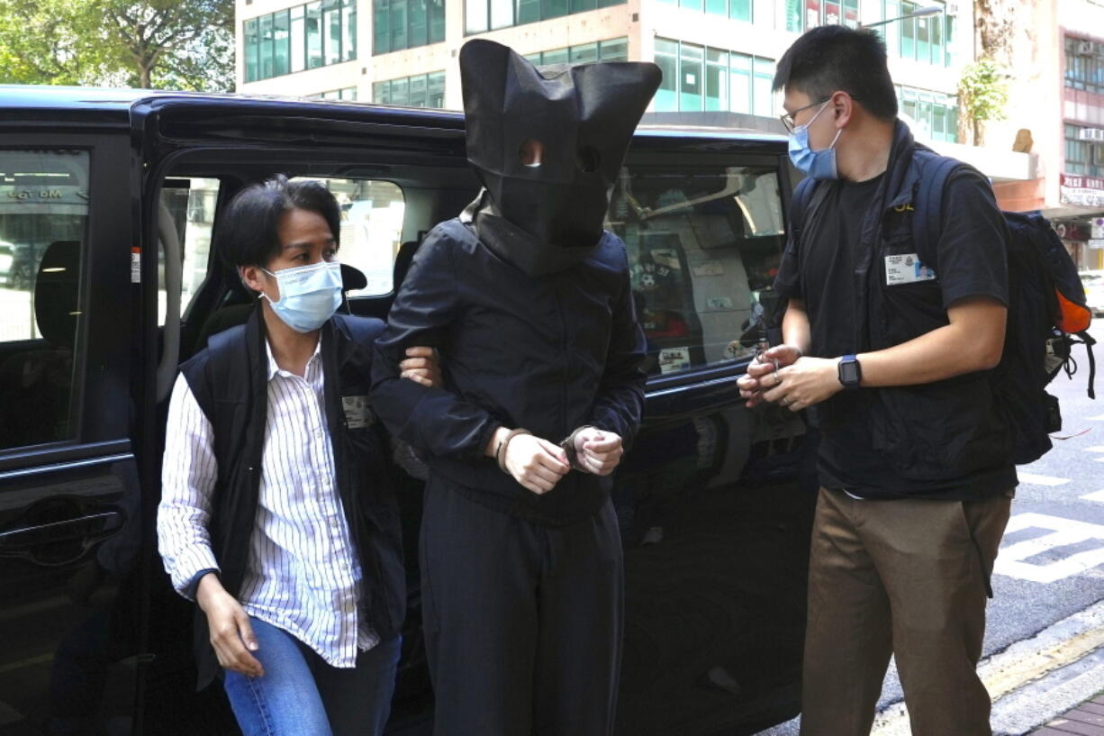 FILE - A hooded suspect is accompanied by police officers to search evidence at office in Hong Kong Thursday, July 22, 2021. Five Hong Kong speech therapists were convicted of sedition on Wednesday after they printed a series of children's books about sheep and wolves that a court said was aimed at inciting hatred against authorities.