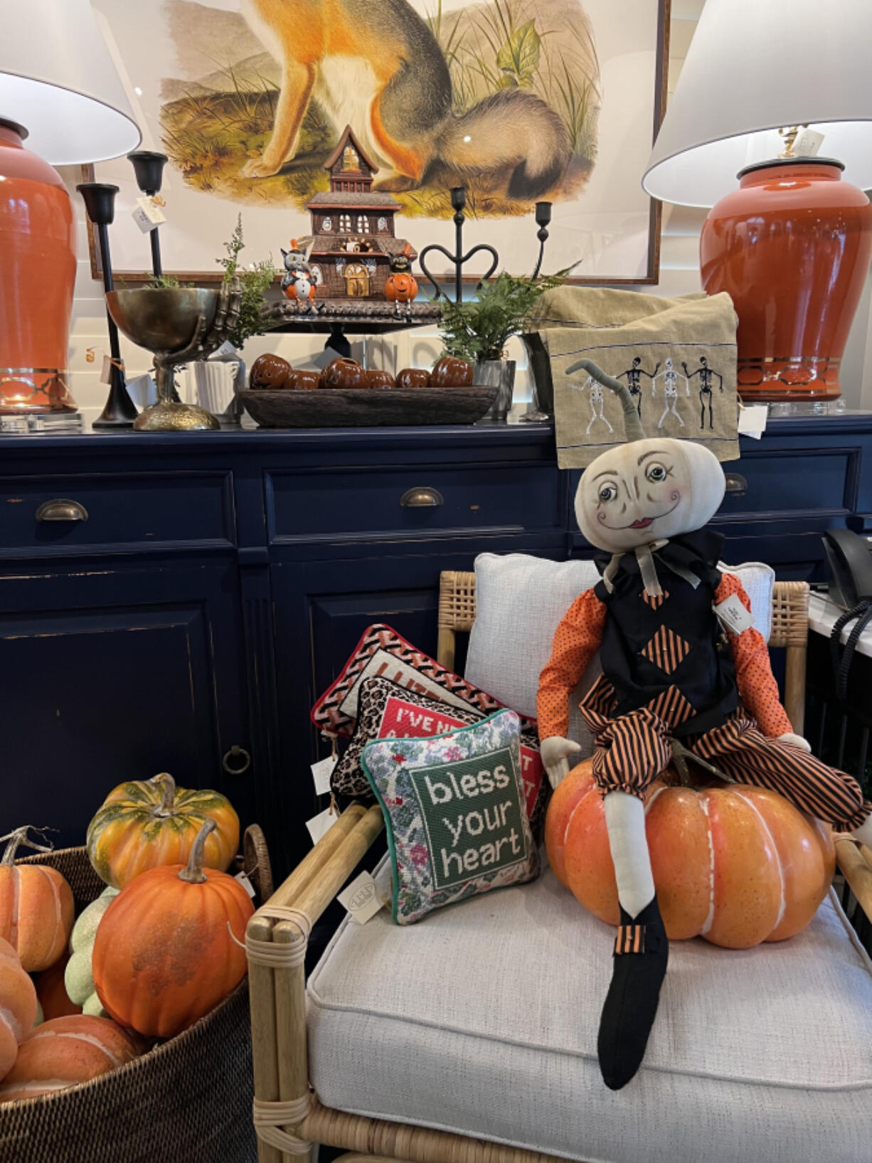 A whimsical pumpkin-headed figure sits atop an orange gourd, surrounded by Halloween decor.