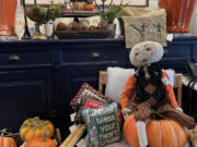 A whimsical pumpkin-headed figure sits atop an orange gourd, surrounded by Halloween decor.