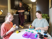 Belle Jackson, 10, left, plays with modeling clay with her mom, Stephanie James, right, as dad Bryant James watches in the kitchen at their home in Vancouver. Belle, who has DiGeorge syndrome, has spent time at home with her parents lately after a rocky start to her school year.