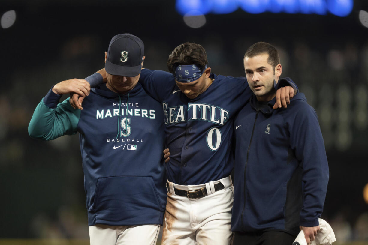 Seattle Mariners' Sam Haggerty, center, is helped off the field by training personnel manager Scott Servais, left, while stealing second base during the ninth inning of a baseball game against the Detroit Tigers, Monday, Oct. 3, 2022, in Seattle. The Tigers won 4-3.