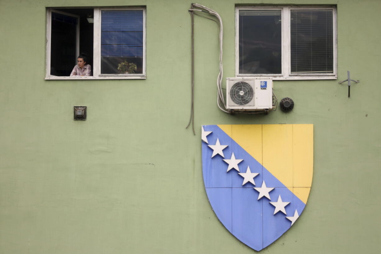 A woman looks through the window next to the giant flag of Bosnia and Herzegovina in Sarajevo, Bosnia, Wednesday, Oct. 12, 2022. Bosnia-Herzegovina moved a small step closer to the European Union on Wednesday with the EU's executive advising member states to grant it candidate member status despite continuing criticism of the way the Balkan nation is run.