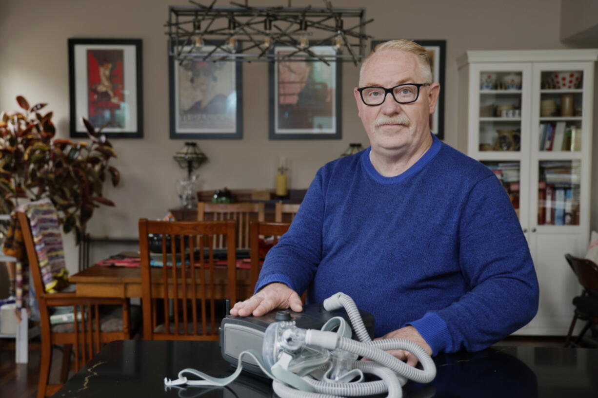 Jeffrey Reed, who experienced persistent sinus infections and two bouts of pneumonia while using a Philips CPAP machine, poses with the device at his home Thursday, Oct. 20, 2022, in Marysville, Ohio. The device is part of a massive global recall of breathing machines triggered by sound-dampening foam that can break down, releasing potentially harmful particles and chemicals.