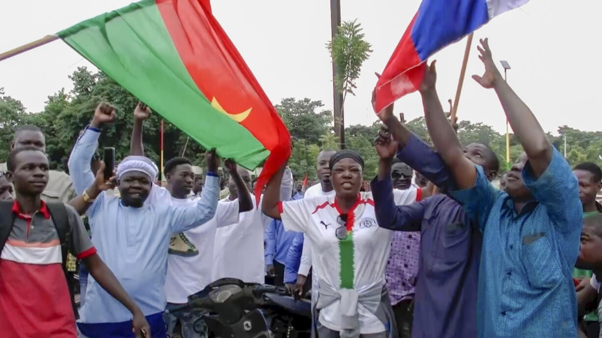 Demonstrators gather near Thomas Sankara memorial with Burkina Faso and Russian flags in support of what they believe to be another military coup in Ouagadougou Friday Sept. 30, 2022. Residents say gunfire rang out early in the morning and the state broadcaster has gone off the air, fueling fears that another coup is underway. The developments Friday come just after coup leader-turned-president Lt. Col. Paul Henri Sandaogo Damiba returned from a trip to the U.N. General Assembly.