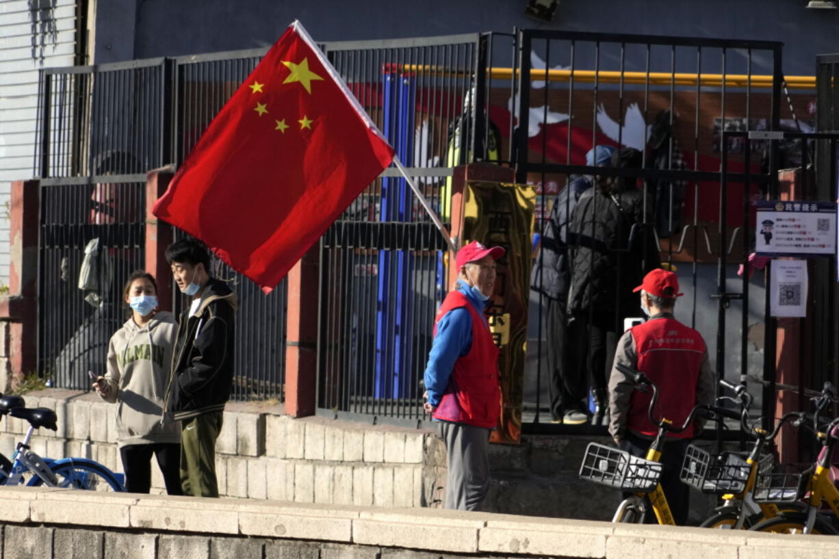 Residents and neighborhood watch members stand near a Chinese flag along a street ahead of the closing ceremony of the 20th National Congress of China's ruling Communist Party in Beijing, Saturday, Oct. 22, 2022.