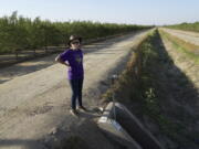 Elaine Moore stands next to a dry irrigation canal and almond orchard near her property, where two wells have gone dry this summer in Chowchilla, Calif., Sept. 14, 2022. Amid a megadrought plaguing the American West, more rural communities are losing access to groundwater as heavy pumping depletes underground aquifers that aren't being replenished by rain and snow.