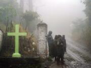 Soldiers stand guard under the rain near a cross that decorates a road in Comasagua, El Salvador, Monday, Oct. 10, 2022. At least five soldiers died on Monday nearby when the wall of a home collapsed as they were sheltering from the rain while deployed to crackdown on gang activity.