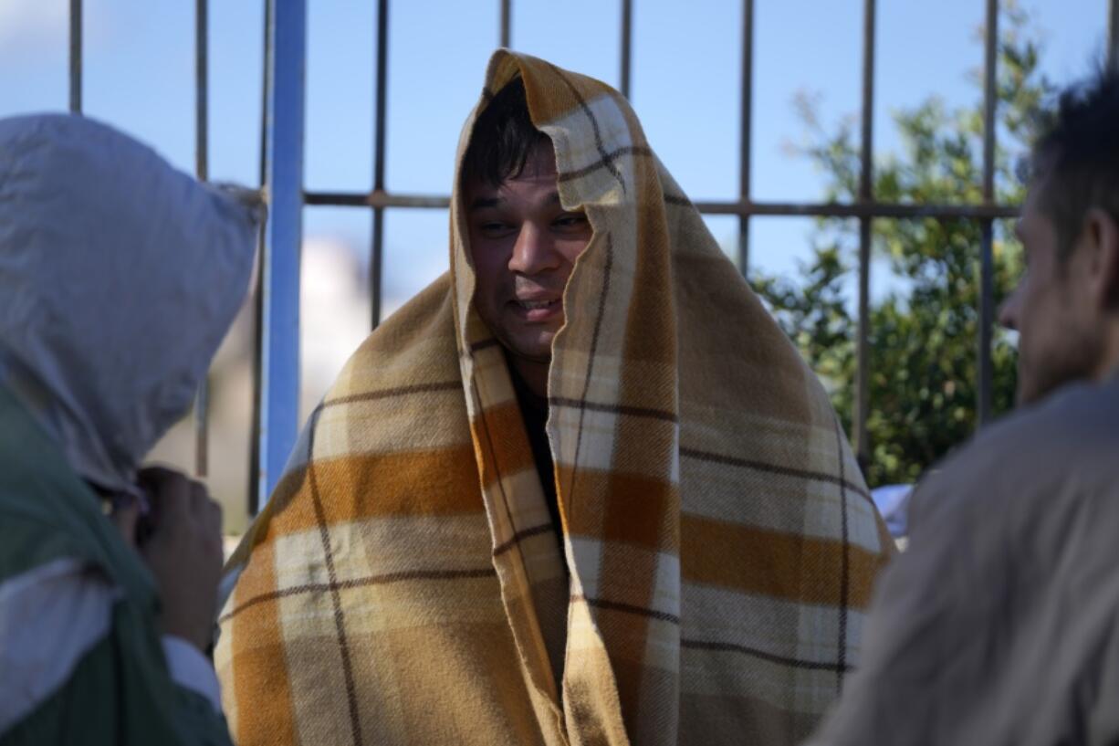 An Afghan covered with a blanket, speaks with other migrants at an old school used as a temporary shelter on the island of Kythira, southern Greece, Friday, Oct. 7, 2022. Strong winds were hampering rescue efforts at two Greek islands Friday for at least 10 migrants believed to be missing after shipwrecks left more than 20 people dead, officials said.