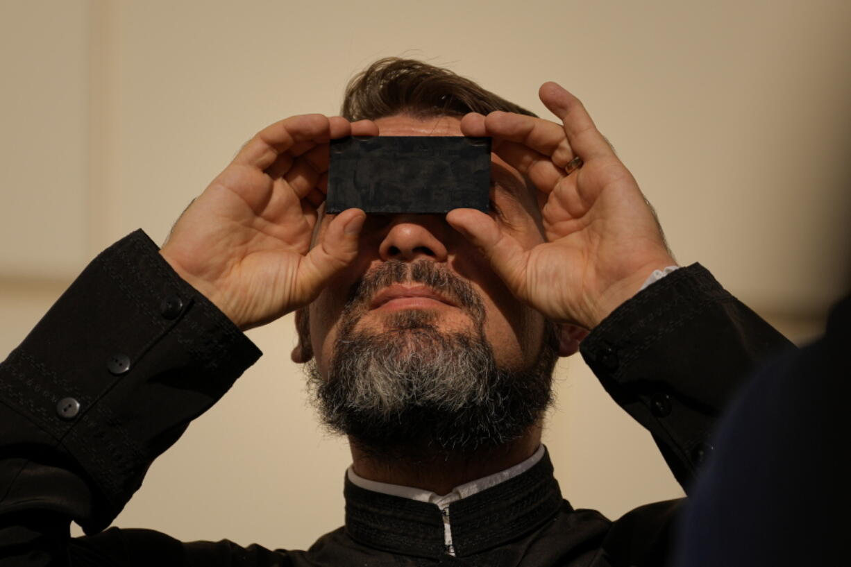 A priest looks through a welding filter during a partial solar eclipse in Bucharest, Romania, Tuesday, Oct. 25, 2022. People around the world gathered Tuesday to witness the last solar eclipse of the year, a phenomenon where the moon briefly casts a black shadow that blocks the sun. It was visible today across Europe, western Asia, northeastern Africa and the Middle East.