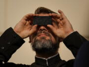 A priest looks through a welding filter during a partial solar eclipse in Bucharest, Romania, Tuesday, Oct. 25, 2022. People around the world gathered Tuesday to witness the last solar eclipse of the year, a phenomenon where the moon briefly casts a black shadow that blocks the sun. It was visible today across Europe, western Asia, northeastern Africa and the Middle East.