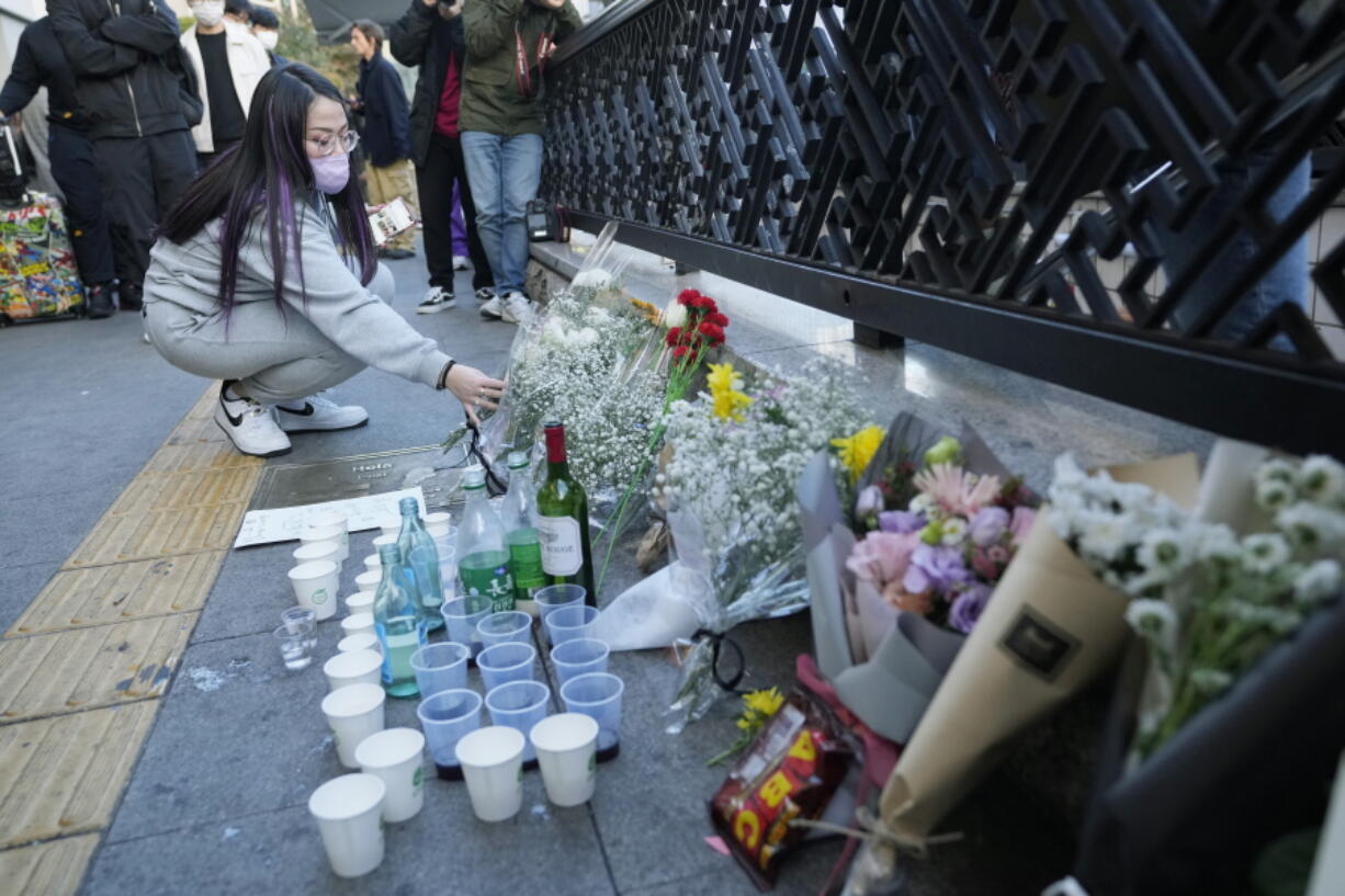 A woman places a bouquet of flowers to pay tribute for victims near the scene of a deadly accident in Seoul, South Korea, Sunday, following Saturday night's Halloween festivities.