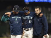 Seattle Mariners' Sam Haggerty, center, is helped off the field by training personnel manager Scott Servais, left, while stealing second base during the ninth inning of a baseball game against the Detroit Tigers, Monday, Oct. 3, 2022, in Seattle. The Tigers won 4-3.