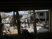 Snowbirds Bruce and Kathy Hickey, both 70, are seen through the windows of a trailer that had been waterfront, as they look at the wreckage of the trailer park where they had a winter home, originally purchased by Kathy's mother in 1979, on San Carlos Island, Fort Myers Beach, Fla., Wednesday, Oct. 5, 2022, one week after the passage of Hurricane Ian.