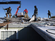 Matrix Roof and Home roofers Alfredo Mendoza, left, and Jorge Gutierrez, second from right, lend a hand as construction continues on the roof of a low-income senior, Lynn, on Wednesday morning. The roof repair enables Lynn to stay in her home after receiving a cease-and-desist notice in September demanding she repair her failed roof within five days.