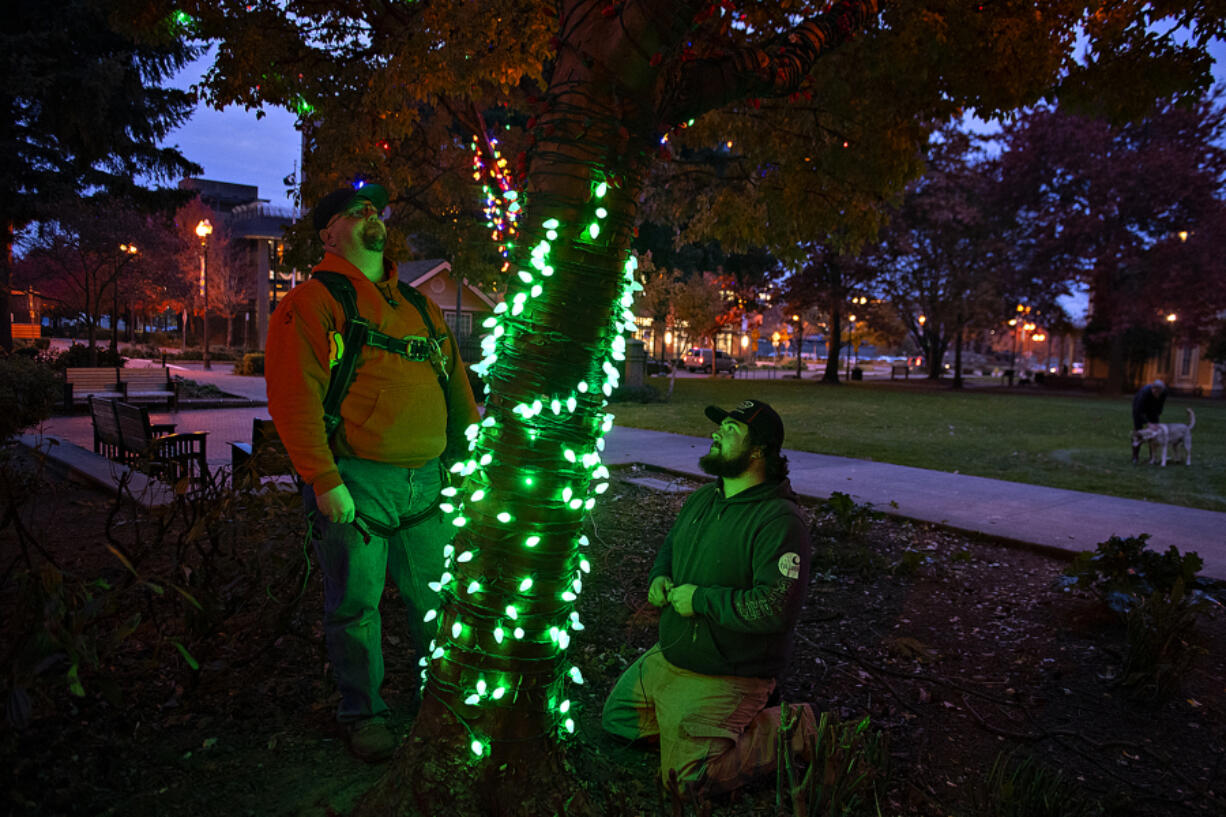 Bryon Ledin of Clark Public Utilities, left, works with colleague Spencer Fix as they test colorful holiday lights at Esther Short Park on Monday afternoon. The Rotary Community Tree Lighting will kick off at 4 p.m. Friday after a two-year hiatus from its in-person celebrations.