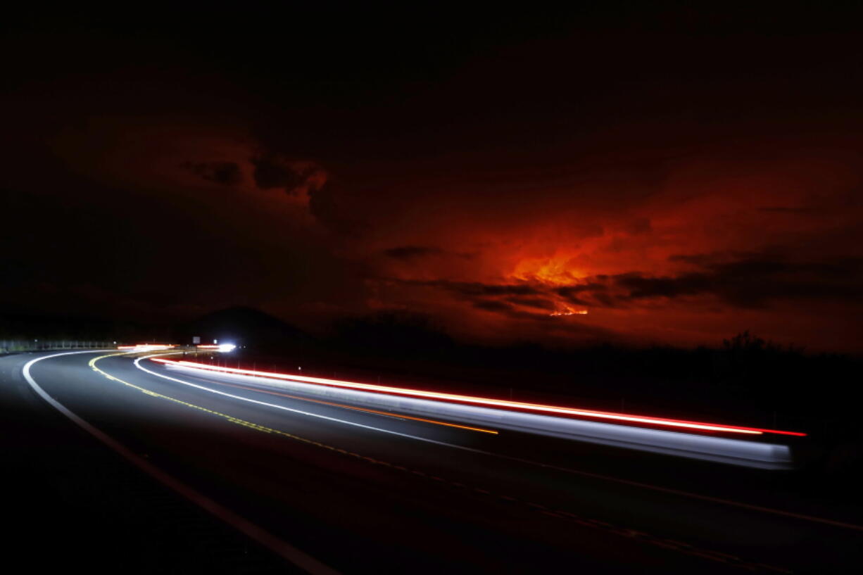 In this long camera exposure, cars drive down Saddle Road as Mauna Loa erupts in the distance, Monday, Nov. 28, 2022, near Hilo, Hawaii. Mauna Loa, the world's largest active volcano erupted Monday for the first time in 38 years.