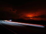 In this long camera exposure, cars drive down Saddle Road as Mauna Loa erupts in the distance, Monday, Nov. 28, 2022, near Hilo, Hawaii. Mauna Loa, the world's largest active volcano erupted Monday for the first time in 38 years.