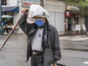 A pedestrian protects his hat from the rain with a plastic bag in the Chinatown district of Los Angeles, Monday, Nov. 7, 2022. A new Pacific storm is bringing snow, rain and wind to California. It's the second significant storm this month for the state, which remains deep in drought.