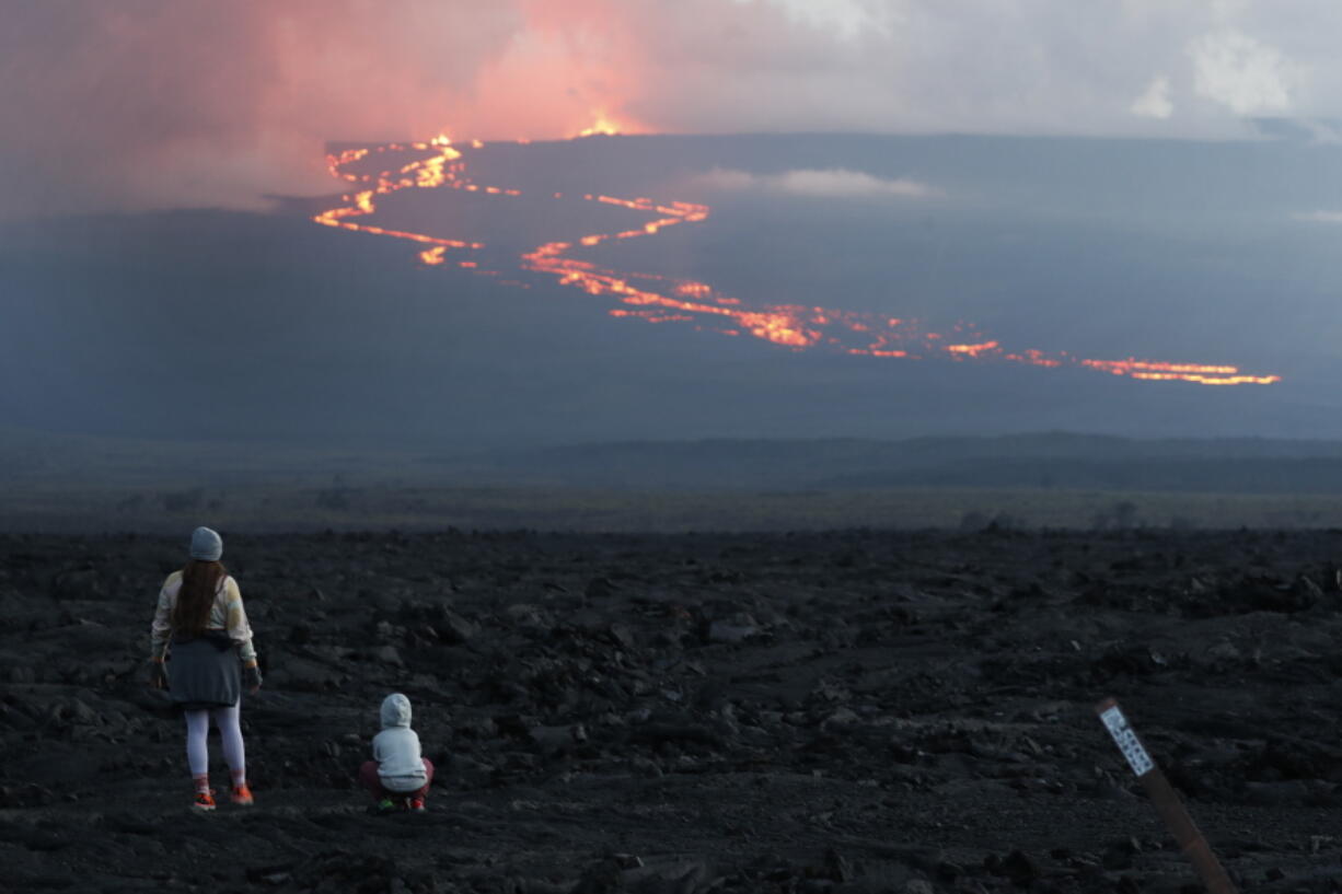 Spectators watch the lava flow down the mountain from the Mauna Loa eruption, Tuesday, Nov. 29, 2022, near Hilo, Hawaii.