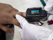 FILE - A health worker uses a pulse oximeter to check the oxygen saturation level of another after administering COVID-19 vaccine at a hospital in Gauhati, India, Jan. 21, 2021. The clip-on devices that use light to try to determine levels of oxygen in the blood are getting a closer look from U.S. regulators after recent studies suggest they don't work as well for patients of color.