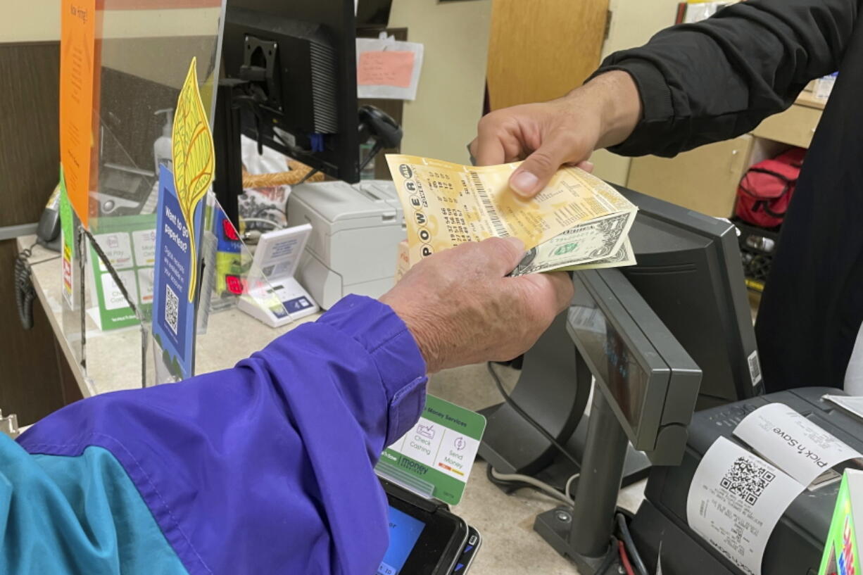 From behind the lottery counter at a Pick 'n Save store in Madison, Wis., Djuan Davis hands Powerball tickets to Arpad Jakab, a retired utility worker who said it's his first time buying them. The Powerball jackpot recently reached a record high of $1.6 billion.