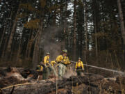 Firefighter Leo Gonzalez, center, sprays smoldering ground in the Camas Creek watershed while working with colleagues to tackle the Nakia Fire on Oct.