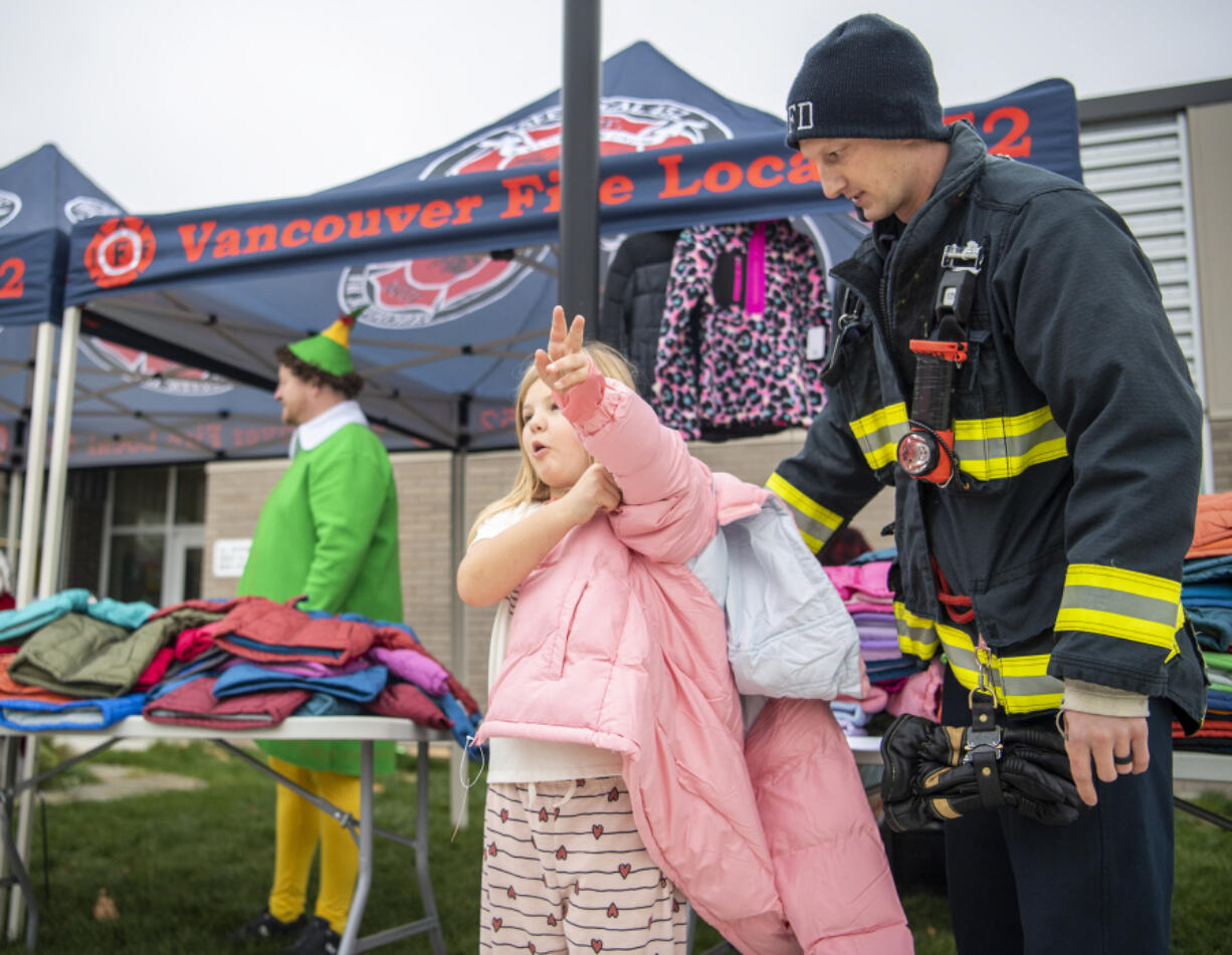 Vancouver firefighter Matt Hankins, right, helps Marshall Elementary second-grader Leilani Beck try on a coat at Marshall Elementary School. Members of Vancouver Fire Local 542 handed out donated coats to students who needed them.