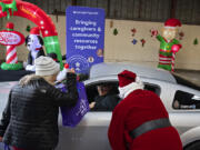 Debbie Russell, left, one of the founders of the annual Caregiver Christmas, greets Asdrual Garcia, son of a caregiver, as he picks up a gift package on her behalf while joined by Santa, also known as Ralph Heiser.