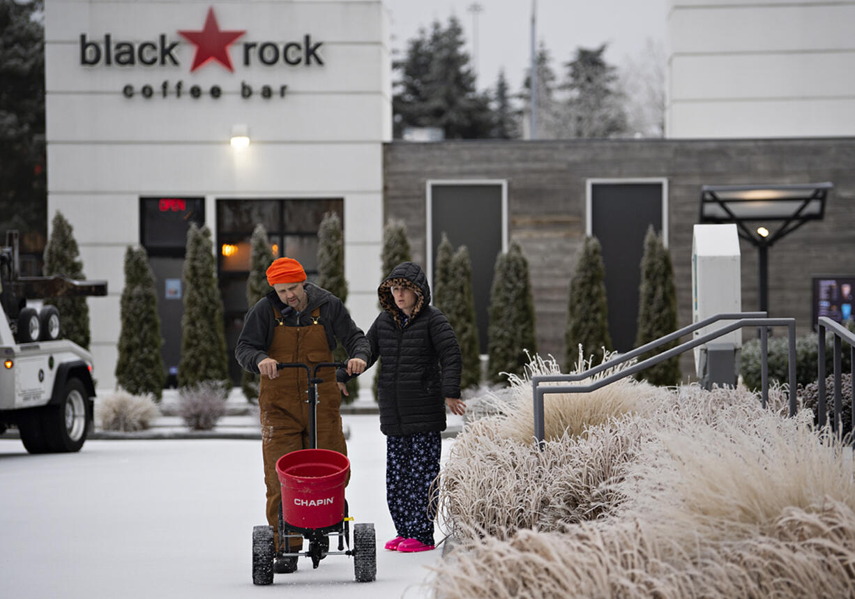 Jerrod Ailshie of Pup Creek Excavation joins his wife, Sara, as they add a layer of ice melting substance around the front pathway of a bank in southeast Vancouver on Friday morning, Dec. 23, 2022. The couple, who live in Woodland, started their day at 4:30 am to help plow roads and help people get around safely.