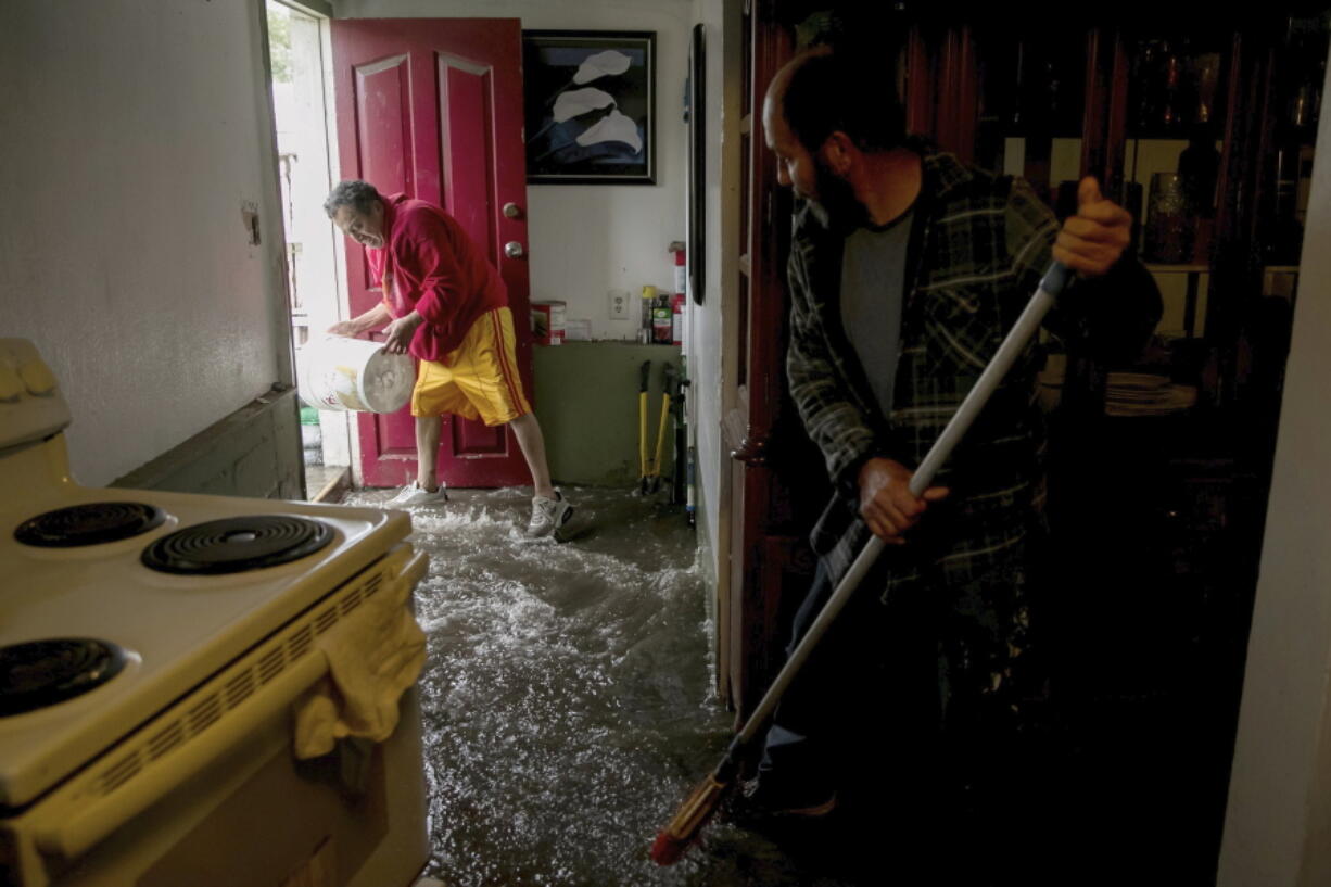 Hugo Archila, left, and Jesus Armando Arredondo use buckets and brooms to clear out water from Archila's home in Seattle's South Park neighborhood Tuesday morning. Jesus Armando Arredondo, who owns the house, says Archila's family had about 2 feet of water in their living room.