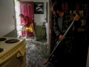 Hugo Archila, left, and Jesus Armando Arredondo use buckets and brooms to clear out water from Archila's home in Seattle's South Park neighborhood Tuesday morning. Jesus Armando Arredondo, who owns the house, says Archila's family had about 2 feet of water in their living room.