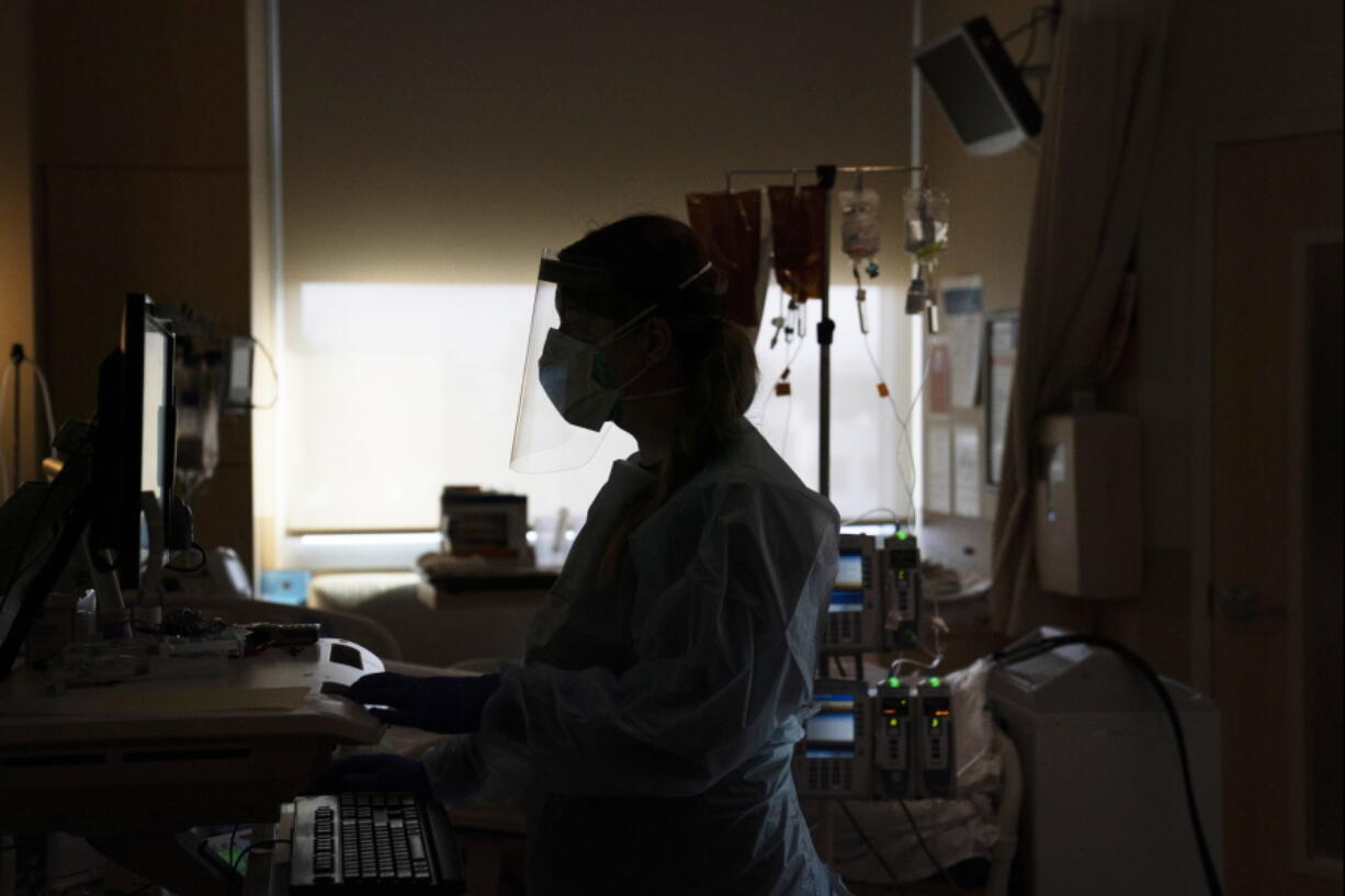 FILE - A registered nurse works on a computer while assisting a COVID-19 patient in Los Angeles. Hospital systems around the country are rolling out fees for some messages that patients send to physicians, saying their providers are increasingly spending more time poring over online queries, some so complex that they require the level of medical expertise normally dispensed during an office visit. (AP Photo/Jae C.