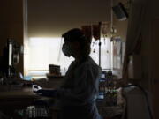 FILE - A registered nurse works on a computer while assisting a COVID-19 patient in Los Angeles. Hospital systems around the country are rolling out fees for some messages that patients send to physicians, saying their providers are increasingly spending more time poring over online queries, some so complex that they require the level of medical expertise normally dispensed during an office visit. (AP Photo/Jae C.